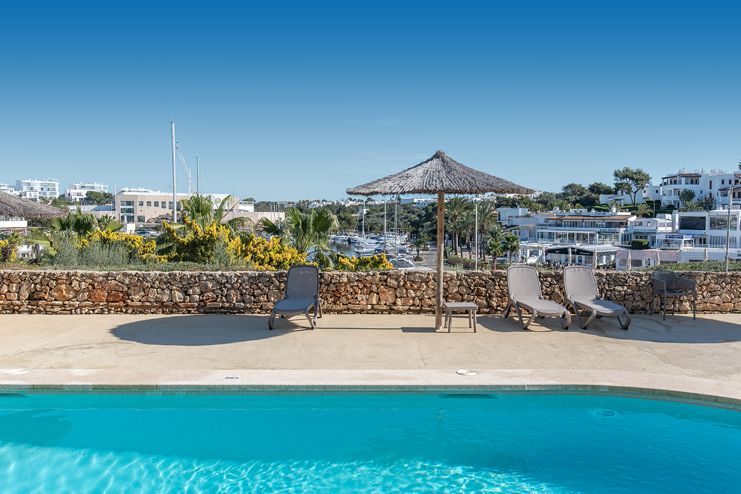 Poolterrasse mit Sonnenliegen und Hafenblick